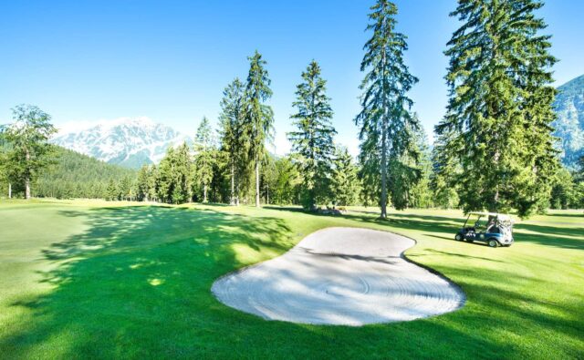 Golfplatz mit Bäumen und Bergen im Hintergrund