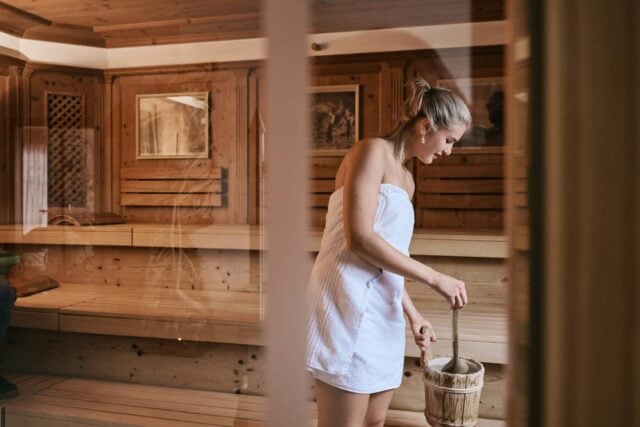 Frau in einer Holzsauna mit einem Eimer