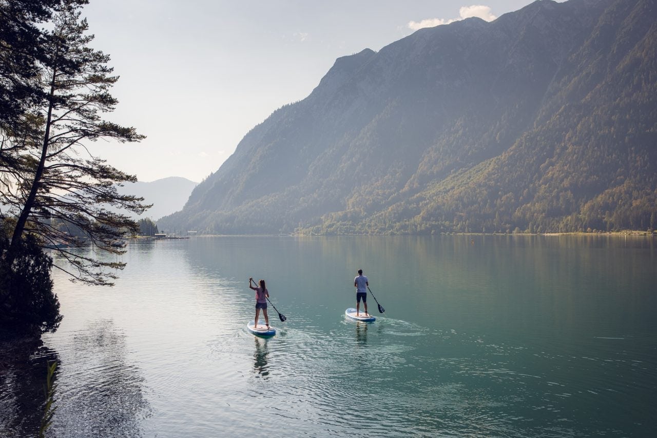 Zwei Personen paddeln auf einem ruhigen See.