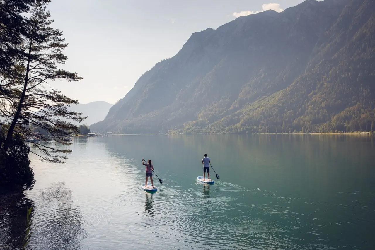 Zwei Personen paddeln auf einem ruhigen See.