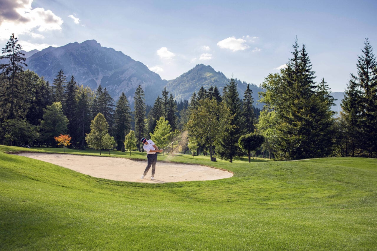 Golfspieler im Sandbunker mit Bergen im Hintergrund