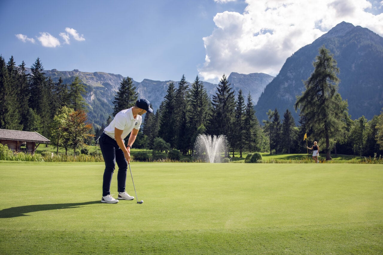 Golfer puttet in malerischer Berglandschaft.