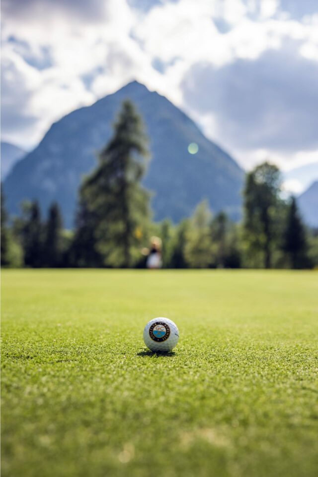 Golfball auf einer grünen Wiese mit Bergen im Hintergrund
