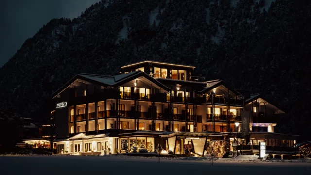 Beleuchtetes Hotel in verschneiter Berglandschaft.